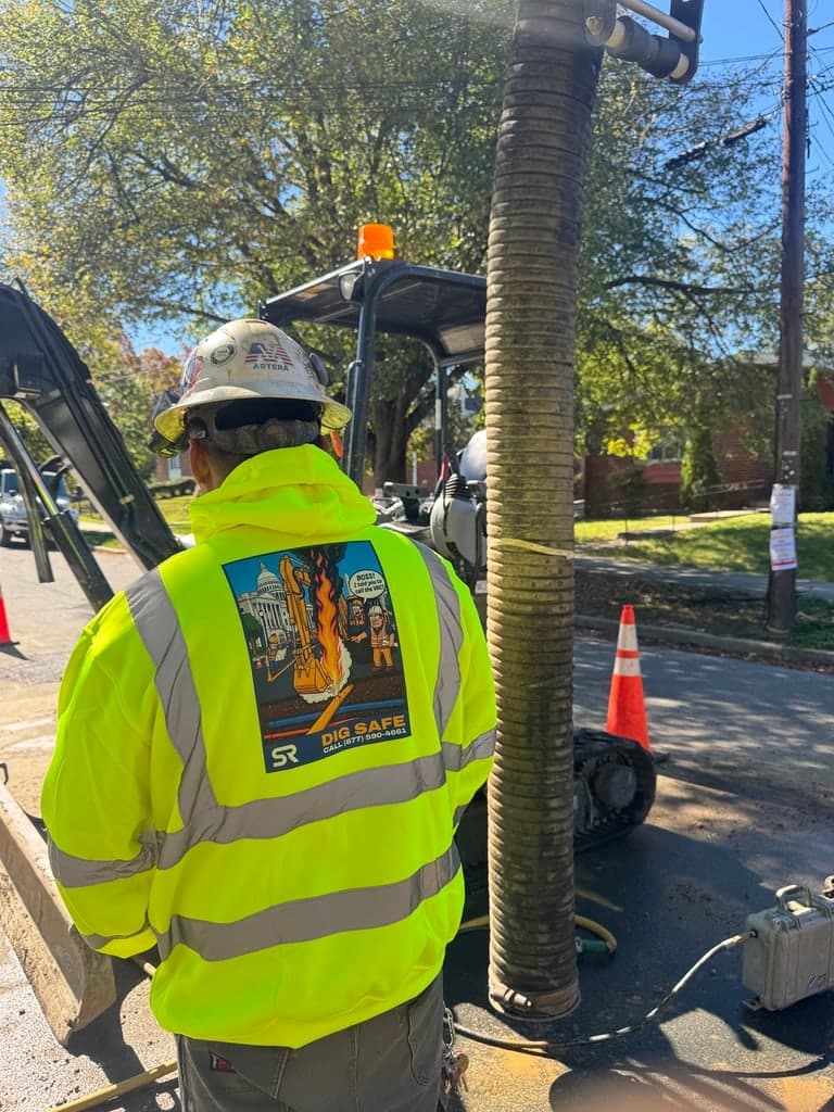 Operator in the Dig Safe hoodie beside a hydrovac hose